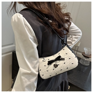 Detail of a chic cream-colored bow shoulder bag worn by a model in a side-rear view