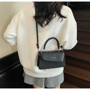Close-up of black crossbody bag with embossed diagonal texture and gold metal logo