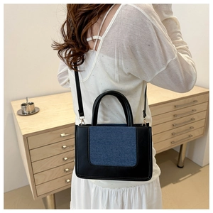 Detail of crossbody bag with black leather frame and blue denim patchwork on a model