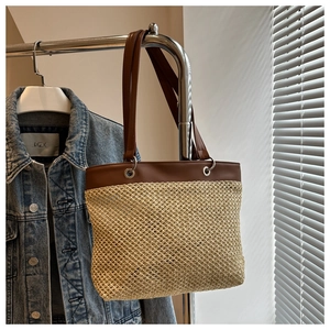 Detail of straw woven tote bag with brown leather straps and metallic rings hanging on a rack