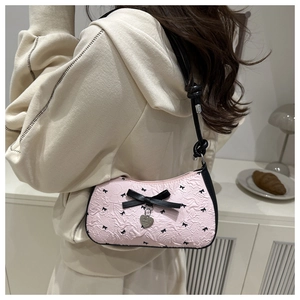 Détail du sac en tissu rose gaufré avec nœuds noirs et pendentif cœur sur la bandoulière