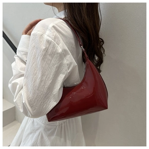 Vista laterale di una donna che indossa una borsa hobo in vernice rosso scuro lucida