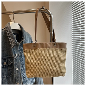 Detail of woven straw tote bag featuring brown leather trim and metal ring connectors