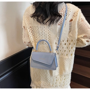 Detailed view of light blue leather bag with woven texture and gold fashion logo