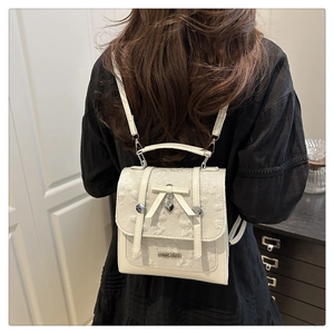 Detail of cream white textured backpack with bow and heart charm on a female model