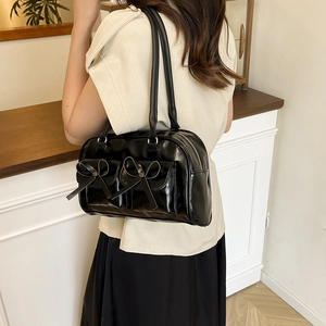 Glossy black patent leather shoulder bag with bow pockets shown on model for daily wear