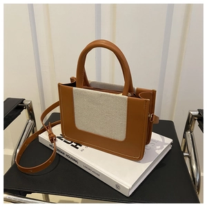 Detail of a chic brown leather and beige canvas crossbody bag on a stack of books