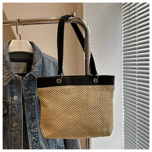 Detail view of woven straw tote bag with black leather straps and silver metal eyelets