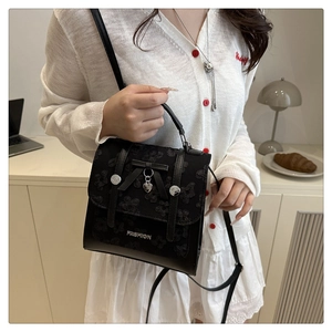 Detail of black lace backpack with heart pendant and bow, styled on white knit cardigan