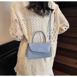 Detail of light blue crossbody bag with woven texture and gold lettering on shoulder