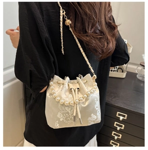 Detail of white floral embroidery bucket bag with pearl handle and golden chain strap