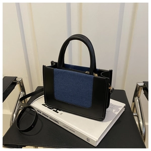 Detail of a chic black leather and blue denim patchwork crossbody bag on a book