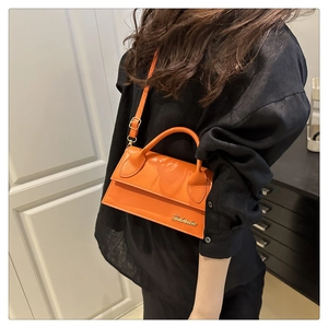 Detailopname van de oranje mini lederen handtas met gouden logo en verstelbare riem