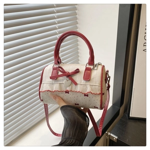 Détail du sac Boston montrant la poignée en cuir rouge, le nœud et le charme cœur