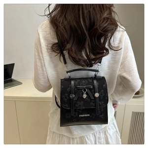 Detail of black backpack featuring 3D floral embroidery, bow, and silver heart pendant