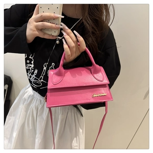 Detail van een roze lederen mini flap tas met goudkleurig logo en groot gebogen handvat