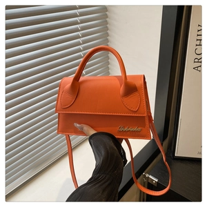 Detail van oranje laks leren crossbodytas met goudkleurig logo en rond handvat
