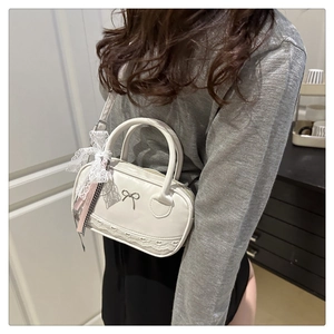 Detail of cream white retro Boston bag with metal bow clasp and lace ribbon charm