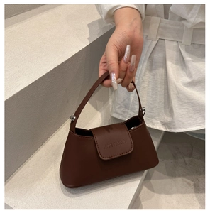 Detail of a brown leather handbag featuring a top handle and embossed logo on the flap