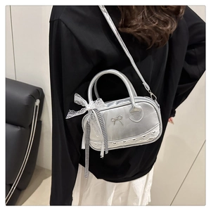 Model wearing a silver bowling bag with bow details and lace trim in a room