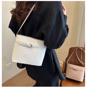 Close-up of white faux leather bucket bag featuring decorative buckle and embossed brand logo