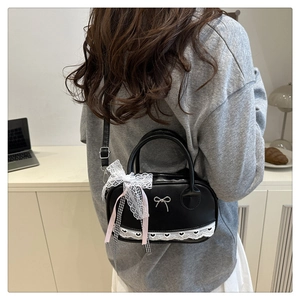 Detail of black PU Boston bag with white lace heart pattern and large bow accessory