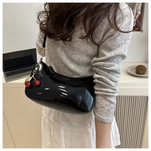Detail of glossy black patent leather crescent bag with realistic red cherry charm