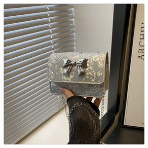 Detail of silver snake-textured mini square bag with metallic bow and chain strap