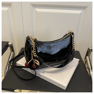 Détail d'un sac à main en cuir verni noir avec chaîne dorée et décoration de cerise