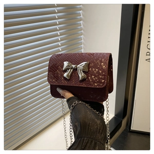 Close-up of wine red faux snakeskin mini bag with a large silver mirror bow detail