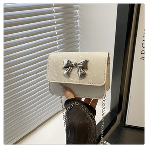 Detail of off-white snakeskin texture with a silver metal bow buckle on a small bag