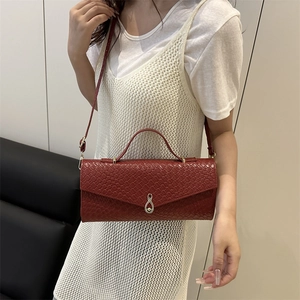 Sac baguette rouge avec texture gaufrée tissée et poignée dorée porté par un mannequin