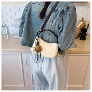 Detail of cream half-moon underarm bag featuring Ailumi 1986 logo and baseball charms