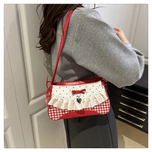 Detail of red and white checkered shoulder bag with bow and heart pendant on model
