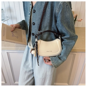 Detail of cream white leather handbag with baseball charm and stylish silk scarf