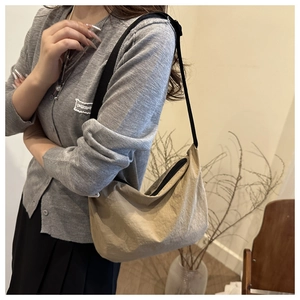 Close-up of minimalist beige hobo bag with black adjustable strap worn by a model