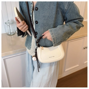 Creamy white half-moon crossbody bag with baseball charm detail shown on a model