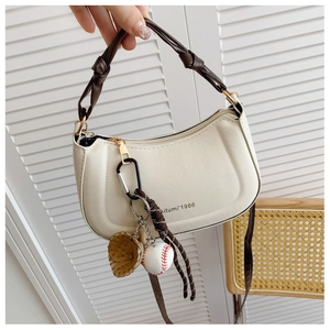 Detail of a chic cream-colored small square bag featuring a brown knotted handle and bag charm