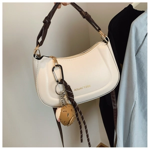 Detail of a creamy white half-moon bag with dark brown twisted handle and baseball pendant