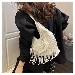 Detail van een witte hobo-tas met lange franjes gedragen door een model in het zwart