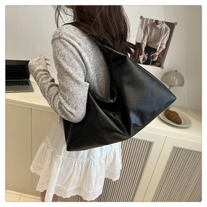 Detail showing the textured black leather hobo bag worn by a model in a cozy indoor setting