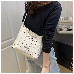 Detail of white textured bucket bag featuring black bow prints and silver heart pendant
