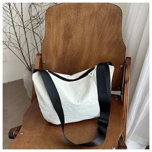 Detail of white nylon crossbody bag with black strap on a wooden chair