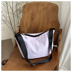 Detail of lavender crescent bag on wooden chair with wide black strap and zipper