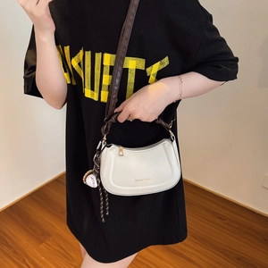 Minimalist white leather crescent crossbody bag with brown strap and baseball charm
