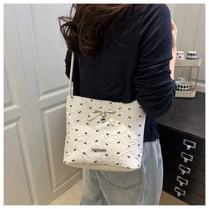 Close-up of white bucket bag with black bow embroidery and heart-shaped metal pendant