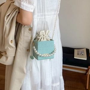 Mint green mini crossbody bag with pearl handle and drawstring shown on a female model