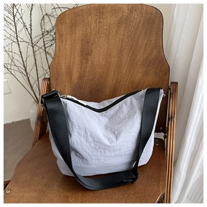 Close-up of light purple nylon crossbody bag with wide black strap on wooden chair
