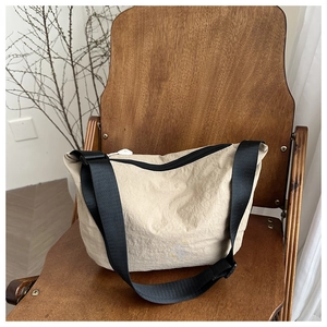 Detail of a beige pleated nylon crossbody bag on a rustic wooden chair with a wide black strap
