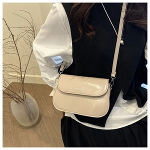 Détail du sac bandoulière beige brillant avec logo et design à rabat incurvé